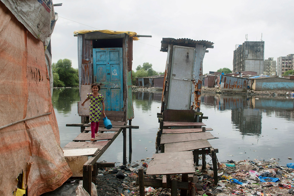 Una niña sale de un retrete hecho sobre pilares de madera, donde los residuos se vierten directamente en una fuente de agua abierta en Mumbai, India.