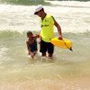 Un joven ayuda a un niño a salir del agua en una playa de Gaza